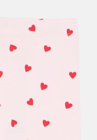 Ανοιχτό ροζ ύφασμα με διασκορπισμένο μοτίβο μικρών κόκκινων καρδιών. Ομαλή υφή με ραμμένη μέση.