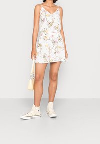 Abito con motivo floreale bianco, con scollo a V e spalline regolabili, vita cintrata e gonna ampia; abbinato a sneakers alte color crema.