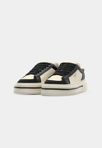 Svarte og kremfargede lær-sneakers med lav design, teksturert overdel, rund tå og en tykk, hvit såle med svarte detaljer.