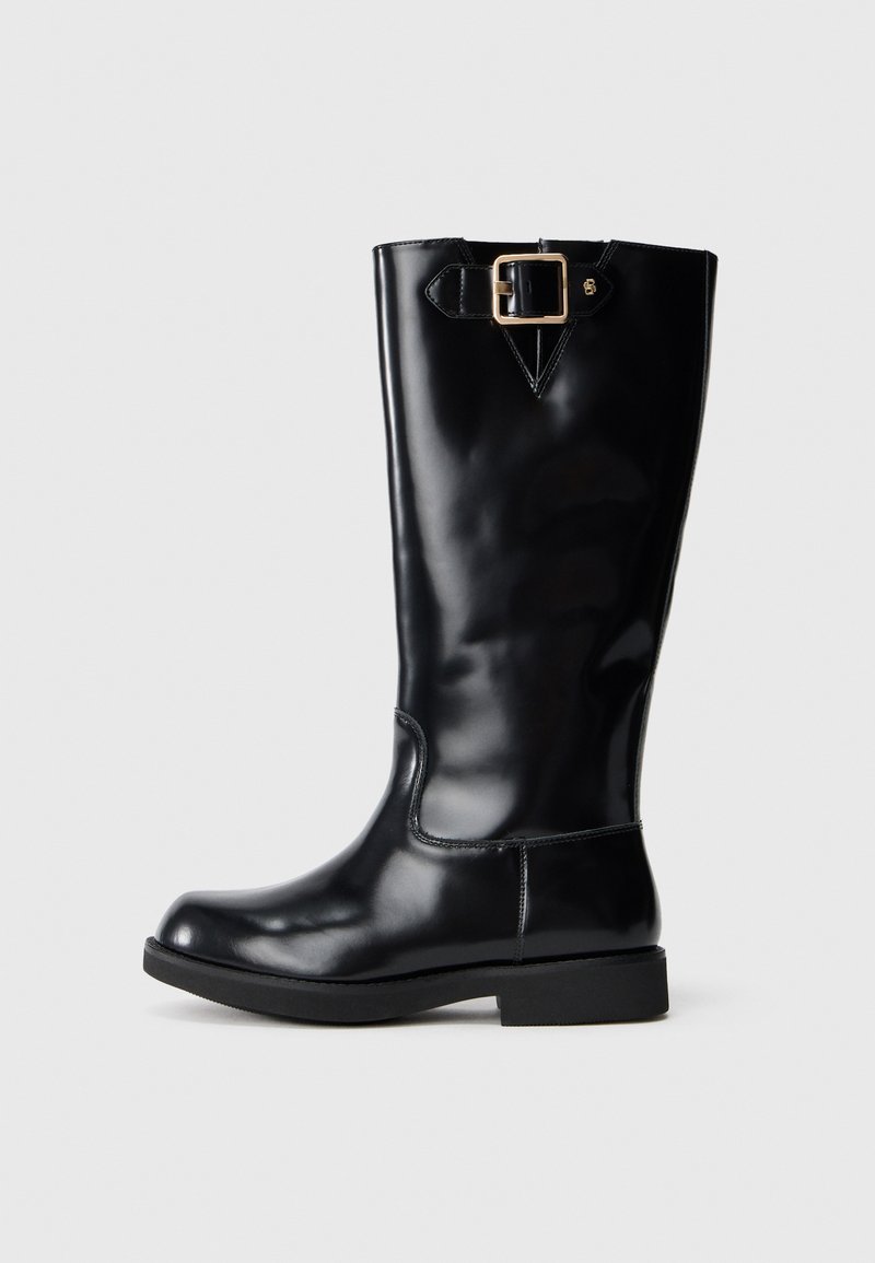 Botas de cuero negras hasta la rodilla con un acabado suave y brillante. Presenta un hebilla lateral, punta redondeada y una suela baja y sólida.