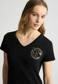 Zwarte V-hals t-shirt van katoen. Voorzien van een goud- en zilverkleurig logo met stipaccenten op de linkerborst. Korte mouwen.