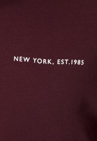 Bordowy pulower z białym napisem "NEW YORK, EST. 1985." Gładka bawełniana faktura, dekolt typu crew neck, styl minimalistyczny.