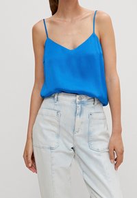 Blaue, strukturierte Camisole mit dünnen Trägern und V-Ausschnitt, kombiniert mit hellblauen, hochgeschnittenen Jeans aus Denim mit Vordertaschen.