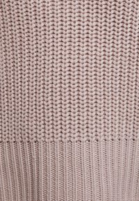 Strickpullover in zartem Rosa mit einem strukturierten Muster aus einer Mischung aus vertikalen und horizontalen Stichen, das ein weiches und gemütliches Erscheinungsbild bewahrt.