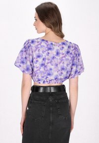 Lilla blomster crop top med puffede ærmer, samlet kant og en glat stof. Bæres med en højtsiddende sort denim nederdel.