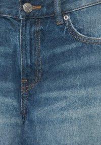 Jean en denim bleu à l'avant avec bouton en métal, couture orange, passant de ceinture et poche avant rivetée.