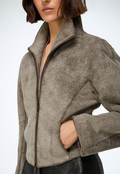 Smeđa jakna od antilopa s patentnim zatvaračem i visokim ovratnikom, s teksturiranim završetkom i bočnim džepovima, prikazana pola zatvorena.