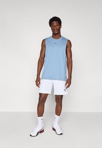 Puma sleeveless athletic shirt in light blue, paired with white shorts. Features a smooth texture and subtle logo on the chest.