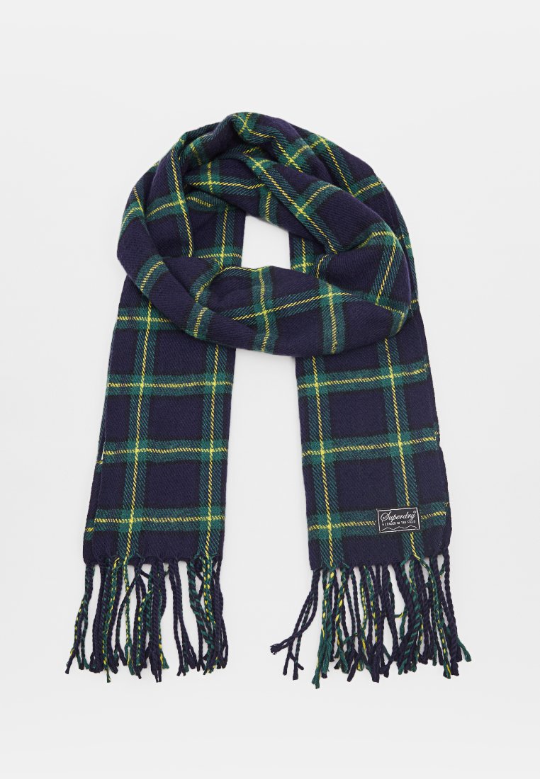 Écharpe en tartan navy avec un motif à carreaux verts et jaunes. Fini avec des bords frangés et une petite étiquette de marque. Texture douce et tissée.