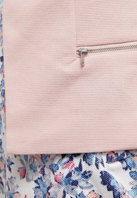 Roze gestructureerde stof met een ritssluiting aan de bovenkant, boven een sectie met een bloemenpatroon in blauw-, roze- en wittonen.
