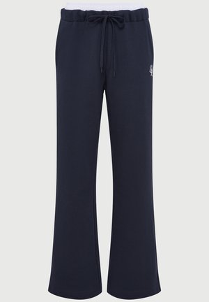 Pantalons de survêtement amples bleu marine avec taille élastique blanche, poches avant, fermeture à cordon et petit logo blanc sur la cuisse droite.