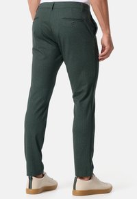 Zielone spodnie o wzorze jodełki, dopasowane, z tylnymi kieszeniami i gładką fakturą, zestawione z jasnymi trampkami.