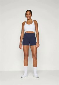 Fehér crop top és tengerészkék magas derekú rövidnadrág. Sima, elasztikus anyag. A modellen fehér sneaker és bokazokni van, egy egyszerű háttér előtt áll.