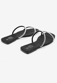 Sandalias planas negras con dos correas entrelazadas adornadas con pequeñas piedras brillantes. Textura suave y suela de forma cuadrada.
