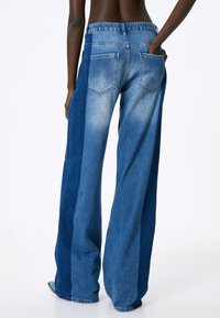 Jeans de pierna ancha hechos de denim, con un diseño bicolor que presenta secciones de azul claro y oscuro, bolsillos traseros y un ajuste relajado.