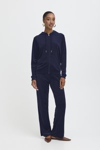 Mörkblå velour träningsdräkt med en zip-up hoodie som har en framficka och matchande vida byxor, tillverkad av mjukt, texturerat tyg.