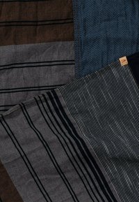 Tissu tissé avec des motifs à rayures dans des tons marron, gris et bleu ; présente des textures fines et une petite étiquette de marque dans un coin.