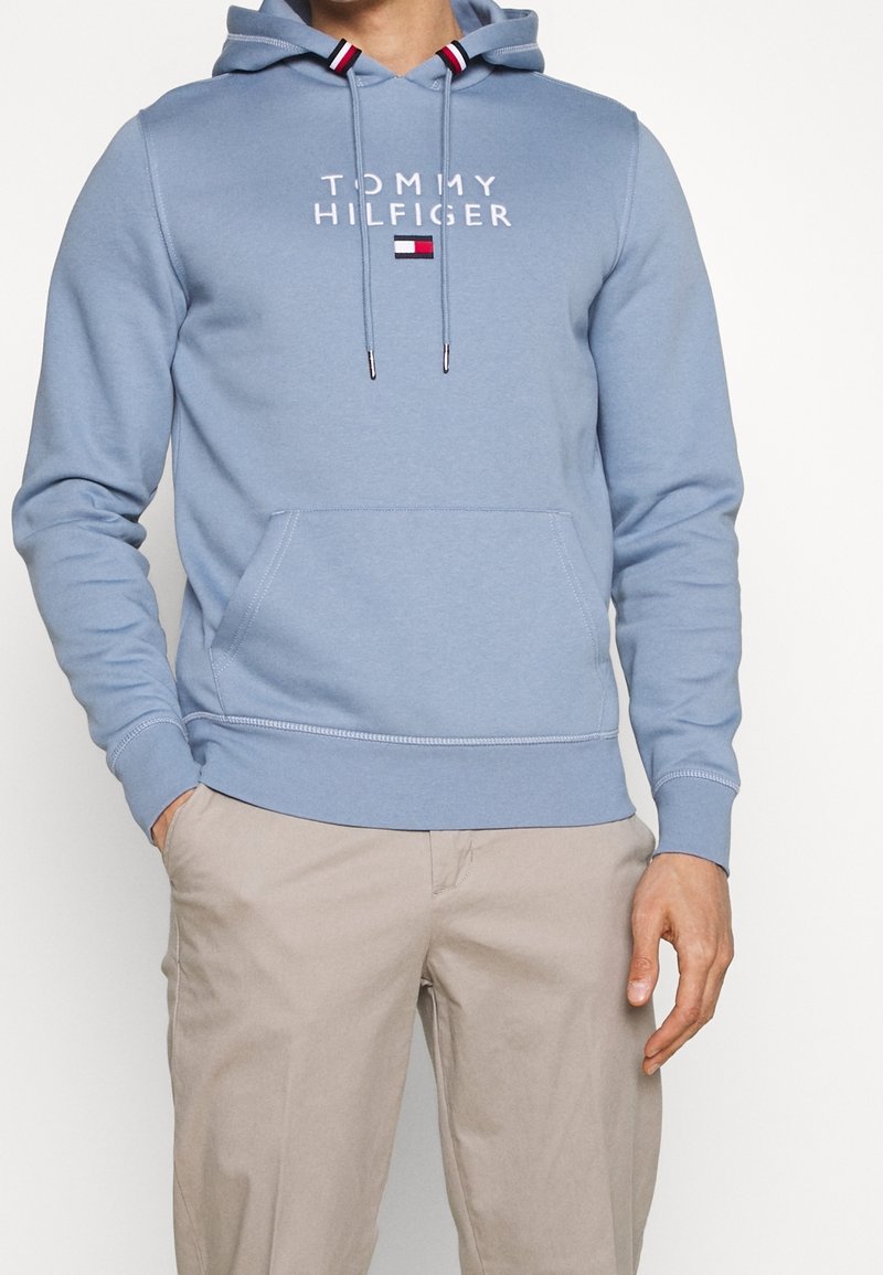 Sudadera de algodón azul claro con un bolsillo frontal, capucha con cordón y logo impreso de "Tommy Hilfiger". Presenta puños y dobladillo acanalados.