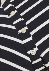 Marinblå och vitrandig tyg med runda, beige knappar. Har en textured stickad design och knappslå.