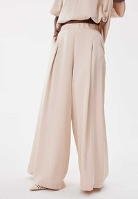 Pantalons à jambes larges en tissu beige doux, dotés de plis avant, d'une taille haute et d'une texture lisse. Couleur solide subtile sans motifs.