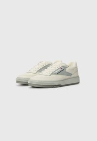 White and gray sneakers featuring a leather and synthetic upper, padded collar, rounded toe, and textured rubber sole with a tread design.