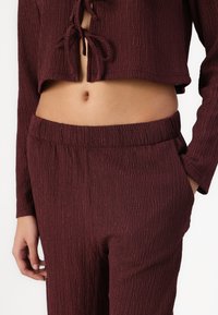 Burgundy cropped top with a textured finish and tie-front detail, paired with matching pants featuring an elastic waistband and pockets.
