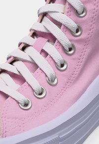 Κοντινή λήψη ροζ πάνινου αθλητικού παπουτσιού με λευκές κορδόνια περασμένα από ασημένια οπές και παχιά λευκή λαστιχένια σόλα.