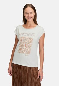 Jasnozielona koszulka z krótkim rękawem z tekstowym wzorem "RADOSNY" z błyszczącymi akcentami, z wzorzystym kwadratem w odcieniach różu i brzoskwini.