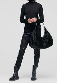 Svart, ribbad polotröja; glänsande, mönstrade svarta byxor; stor, fluffig svart axelväska med kedjehandtag; svarta kängor.