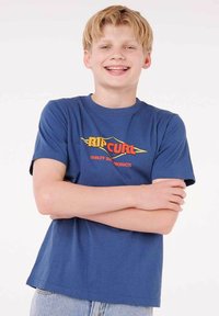 Blaues Baumwoll-T-Shirt mit einem gelb-roten "Rip Curl"-Logo und dem Text "Quality Surf Products", kurzen Ärmeln und einem klassischen Schnitt.