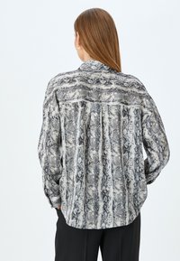 Camisa abotonada con estampado de serpiente en blanco y negro. Corte holgado con mangas largas, cuello y detalle de pliegues en la parte trasera. Textura de tela suave.