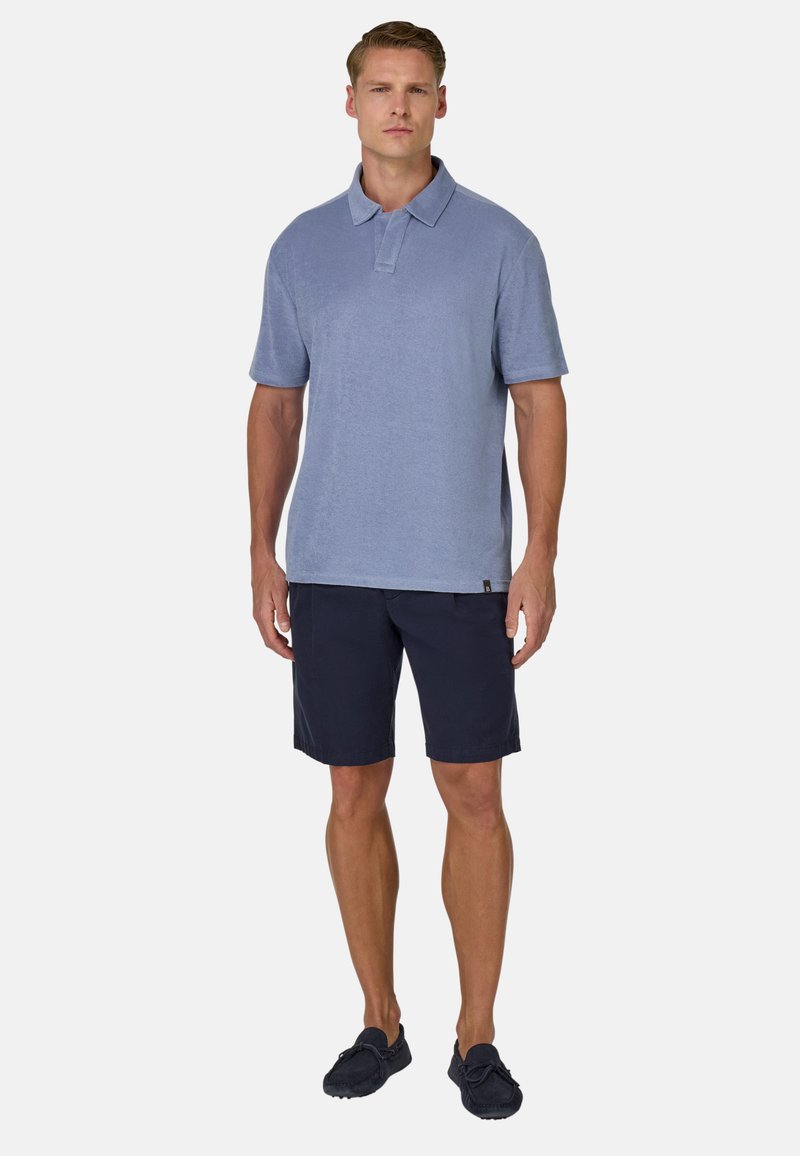 Polo bleu clair avec col, manches courtes, associé à un short marine. Coupe décontractée et texture lisse. Des chaussures foncées complètent le look.