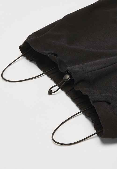 Fekete szövet húzószájú táska, összegyűrhető nyílással, két zsinórzár részlettel és sima textúrával.