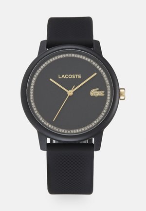 Montre Lacoste noire avec un cadran rond, un cadran rehaussé de cristal, des aiguilles dorées et un bracelet en silicone noir texturé.