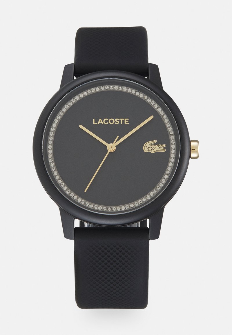 Relógio Lacoste preto com um mostrador redondo, bisel com cristais, ponteiros dourados e uma pulseira de silicone preta texturizada.