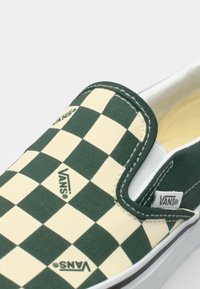 Grüne und cremfarbene Schachbrett-Slipper mit Vans-Logo, Obermaterial aus Canvas, weiße Gummisohle und kontrastierende Nähte.