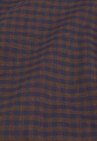 Hnědá a námořnická modrá kostkovaná tkanina s jemnou strukturou, vyznačující se mřížkovým vzorem se střídajícími se čtverci v kontrastních barvách.