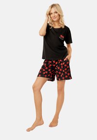 Czarna bawełniana koszulka z krótkim rękawem i grafiką wiśni na piersi, zestawiona z czarnymi szortami w intensywny czerwony wzór wiśni.