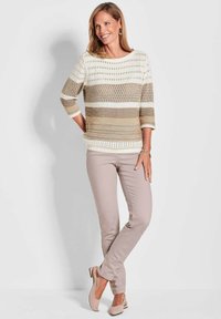 Beige en crème gebreide trui met een open weefpatroon, gecombineerd met lichtbeige slim-fit broek en nude flats, met een soepele textuur.