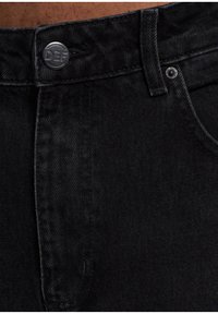Jeans in denim nero con chiusura a bottone con incisione "DEF", cuciture in evidenza e una texture liscia.