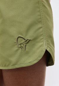 Shorts en tissu vert olive avec ourlet incurvé et logo brodé d'un visage d'animal stylisé sur le côté gauche au-dessus de la cuisse.