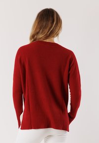 Maglione rosso lavorato a maglia con orlo e polsini a coste. Presenta una vestibilità rilassata e una consistenza morbida. La vista posteriore mostra un profondo scollo e maniche lunghe.
