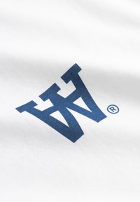 Hvidt bomuldsstof med en blå stiliseret logo med et registreret varemærkesymbol. Teksturen virker glat og blød.