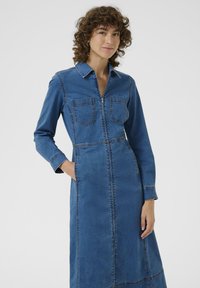 Rochie din denim cu guler, mâneci lungi și fermoar în față. Albastră cu cusături contrastante, având două buzunare la piept și cusături laterale.