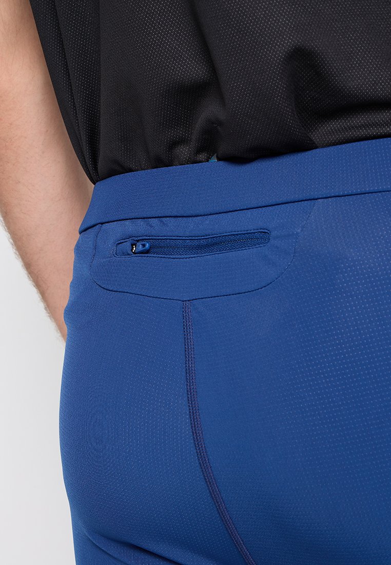 Niebieskie sportowe spodnie z teksturowanej tkaniny, z małą zamek błyskawicznym na plecach i gładkim pasem, w połączeniu z czarną bluzką.