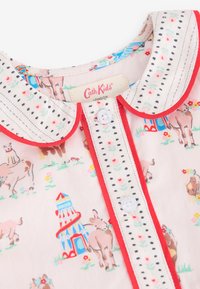 Camiseta infantil de color rosa claro con estampado de vaca y circo, cierre de botones blancos, cuello y ribete rojos, con tela de acento de lunares.