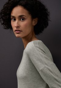 Světlý šedý pletený svetr s kulatým výstřihem a texturovanými akcenty na ramenou. Materiál působí měkce s jemným melírovaným vzorem.