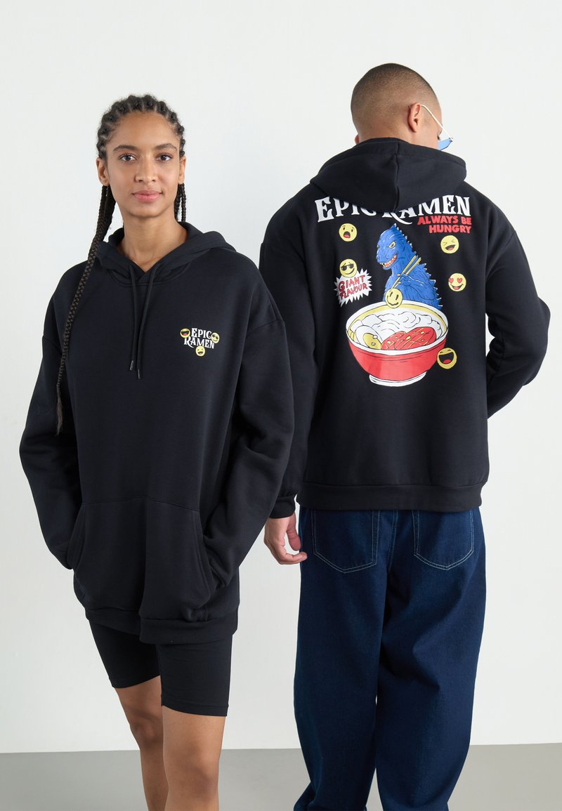Sweatshirts pretos oversized apresentam um bolso frontal e um gráfico de ramen e um monstro nas costas, acompanhados de texto colorido e emojis.