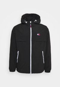 Czarna kurtka z kapturem wykonana z lekkiego materiału, z przednim zamkiem błyskawicznym, dwoma bocznymi kieszeniami i naszywką z logo na piersi. Białe akcenty.