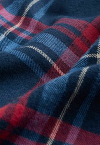 Tissu doux avec une vue en gros plan d'un motif tartan écossais bleu, rouge et blanc, montrant la texture et les couches pliées.